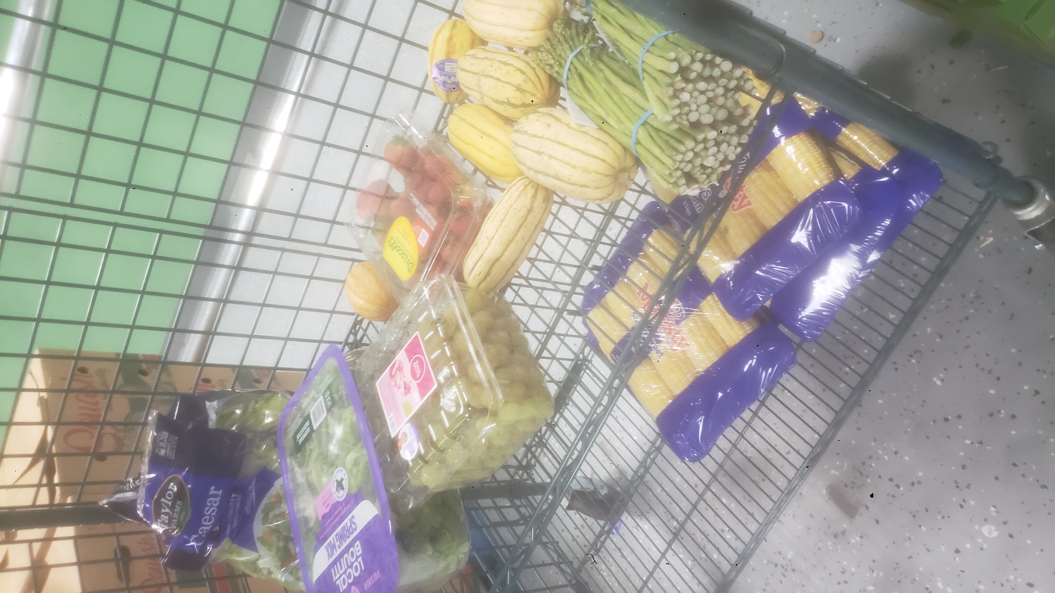 Produce such as grapes and corn on shelves of a cage cart.